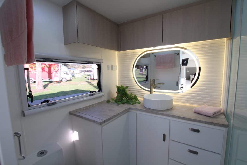 Seascape Sunrunner caravan interior showing an L-shape benchtop in the corner bathroom, featuring ribbed pannelling behind the backlit oval mirror.