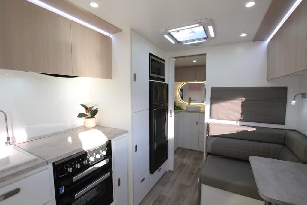 A Seascape Sunrunner caravan interior showing half the galley kitchen and dinette, with the attractive ensuite in the background. Note the top of the cabinets continue onto the ceiling, separated by soft perimeter lighting 