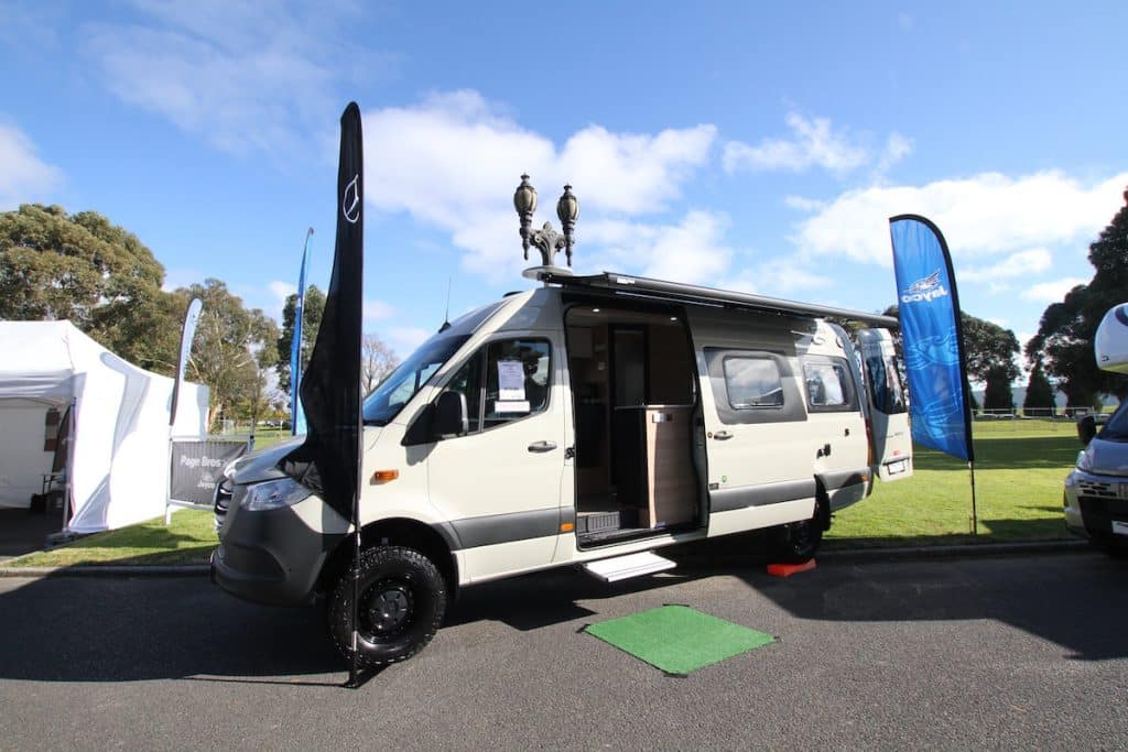 A camel-coloured converted Mercedes campervan, riding high on off-road AWD suspension. 