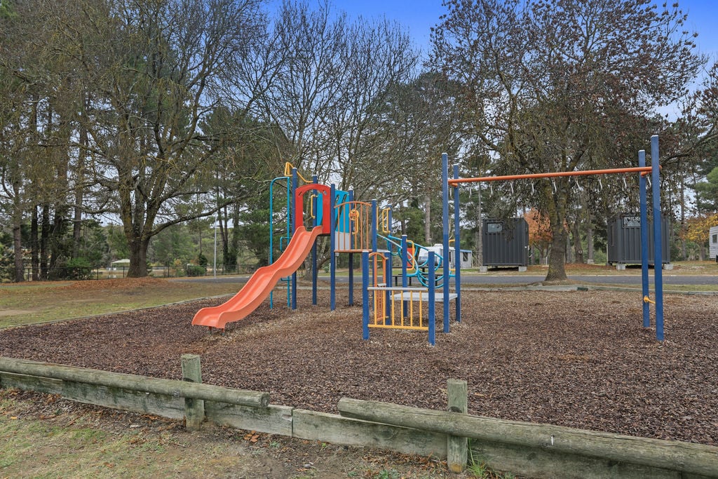 Colourful playground equipment on woodchip ground at Creswick Holiday Park, perfect for family fun.